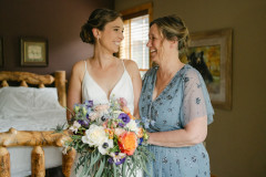 bride holding bouquet standing with mother in room with a bed in it.