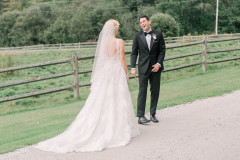 Bride in white dress. Groom in black tuxedo. First look reaction by pasture.