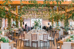 Event barn showcasing greenery, with white table rounds and greenery on tables along with floral arrangements.