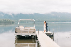 bride and groom on dock overlooking lake with pontoon boat to their left.
