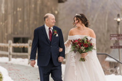Winter wedding featuring bride being walked down the path to the terrace holding a red bouquet