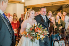 photo of bride in loft with floral bouquet being walked down the aisle by her father.