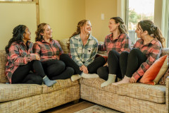 bride in green flannel sitting on sofa with four other women in red flannels sitting around her. 