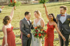 bride and groom in center holding florals smiling at each other with bridesmaids on either side smiling.