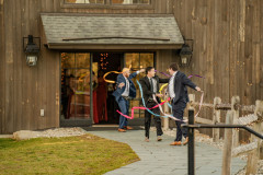 flower men coming from barn holding ribbon sticks waving them around as they walk towards the terrace for a wedding. 