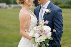 bride and groom standing in front of grass holding bouquet.