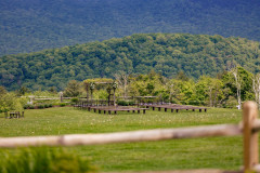 Landscape photo of wedding knoll featuring farmhouse benches and tables with mountainscape in the background.