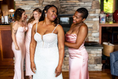 Bride in white while bridesmaid in pink dress helps her zip up dress.