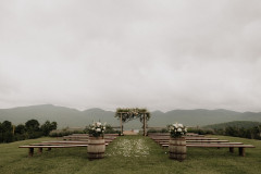 photo of wedding knoll with whiskey barrel floral arrangements and farmhouse benches lining the aisle.