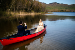 bride and groom in red canoe in lake with mountains in the background.