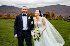 photo of bride and groom with floral bouquet laughing in front of wedding knoll and fall foliage on mountains