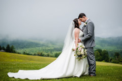 bride and groom in meadow holding each other with fog overlooking the mountains.