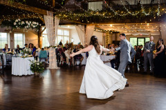 bride and groom dancing in event barn with people around the exterior of the photo and string lighting.