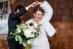 bride and bride holding hands while one does a spin. bride 1 is holding a floral bouquet and is wearing white and bride 2 is in a suit.