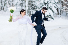 bride and groom holding hands with floral bouquet up in air with winter scape behind them