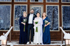 bride and groom with mother of bride and mother of groom standing in front of glass windows with leading staircase.