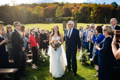 bride and father of bride walking down aisle of wedding knoll with guests on both sides on farmhouse benches
