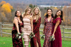 bridesmaids standing together in front of fall view together in red themed dresses holding bouquets.