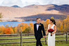 bride and groom walking along next to wooden fence with foliage in the background.