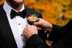 boutonniere of orange and red greenery being pinned on the groom.