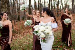 bride holding a white floral bouquet walking towards the camera with four bridesmaids in the background. all are holding smaller white bouquets.