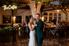 bride and groom in event barn holding hands while doing their first dance. drapery, lights, and greenery surround them with guests in the background in the event barn.