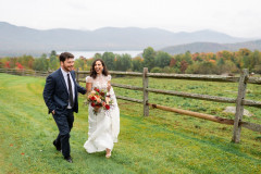 bride and groom walking towards camera next to horse pasture