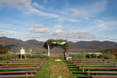 fall wedding ceremony site featuring a wooden arbor with drapery and farmhouse benches lining the aisle