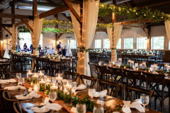 interior if wedding barn for an indoor reception, featuring drapes, table settings, and greenery.