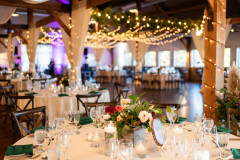 interior setup of event barn for a wedding reception featuring white table rounds with chivari chairs and bright colored floral centerpieces.