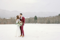 bride and groom kissing in front o f mountain scape with large floral bouquet.