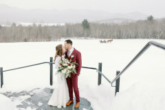 bride and groom standing on staircase outside with sleigh ride passing in background