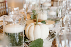 close up of white pumpkin on table for wedding reception with glasses surrounding and candle votives.