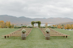 wedding knoll in fall with floral bouquets on top of whiskey barrels in front of farmhouse benches. background features lake and mountains with foliage.