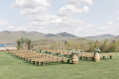photo of wedding knoll with green mountains behind it and farmhouse benches in front with two whiskey barrels with flowers on top of them.