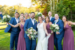 bride and groom standing in the middle of bridesmaids in purple dresses and groomsmen in blue suits.