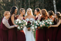 bride and seven bridesmaids in red dresses leaning in holding bouquets. Bridal bouquet features red flowers while bridesmaid bouquets only have pink and white flora.