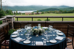 small gathering featuring a table round with a blue tablecloth and a floral centerpiece overlooking a lodge and mountains.
