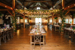 event barn set up for a boho style wedding in september featuring lighting, greenery, and farmhouse tables.