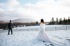 first look of bride walking up to groom with wooden fence and mountains in background.