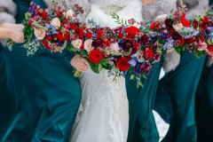 floral bouquets being held by bride and three other bridesmaids in teal. floral bouquets show red roses, pink, blue, and purple floral arrangements.