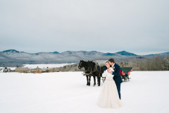 bride and groom in front of horse drawn sleigh and mountain scape.