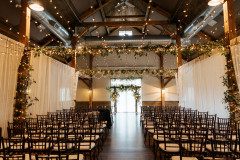 Indoor wedding at event barn featuring ceremony arbor with chairs.