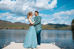 photo of bride and groom at end of dock with lake and green mountains behind them in the background.