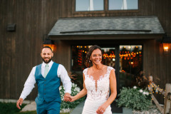 bride and groom walking towards camera smiling with brown event barn in the background.