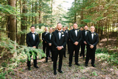 groomsmen party in the woods. all men are wearing black suits and are staggered in the photo.