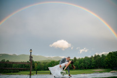 bride and groom kissing under a rainbow on a rainy day at the lodge.