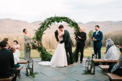 bride and groom kissing in front of round arbor with greenery in the fall.