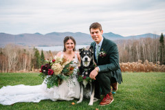 bride and groom smiling with dog with a large bouquet.