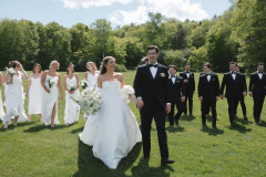 bride and groom walking towards camera smiling with their wedding party behind them also walking towards the camera.